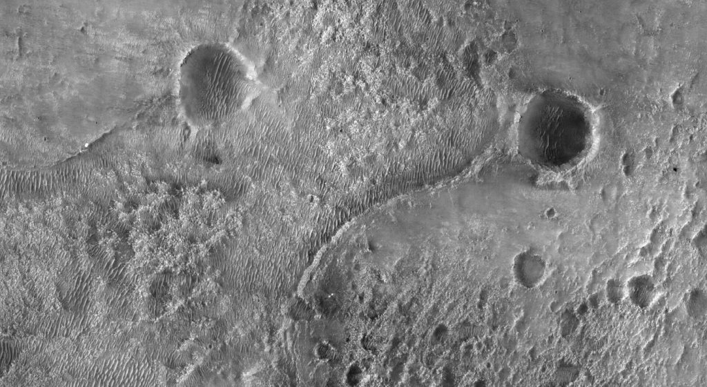 Flexible Mesh Wheels Could Help Mars Rovers Drive Farther A rover traversing the red rocky surface of Mars with layered terrain and a dusty horizon behind it.